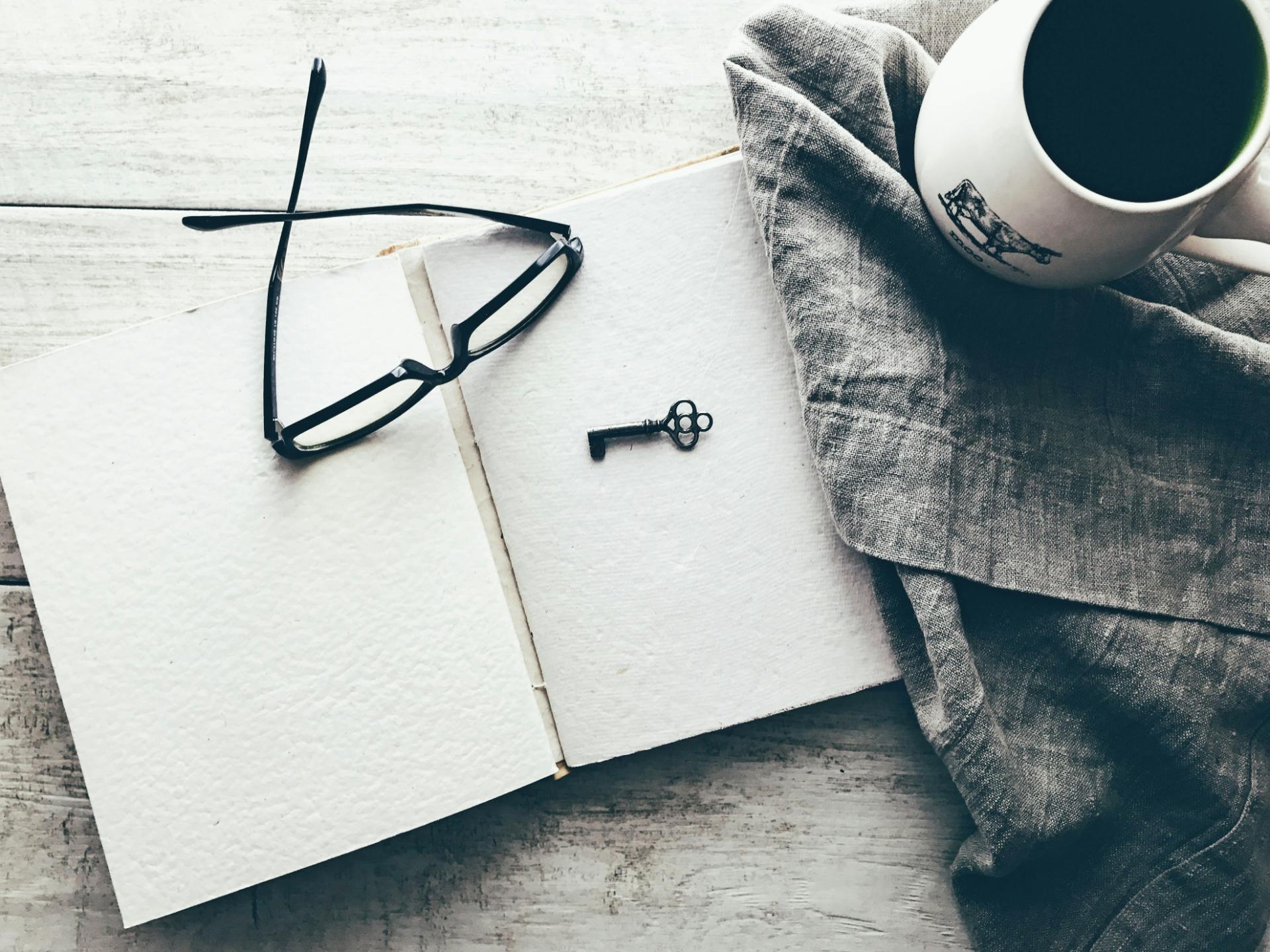 Open notebook with key, glasses, coffee